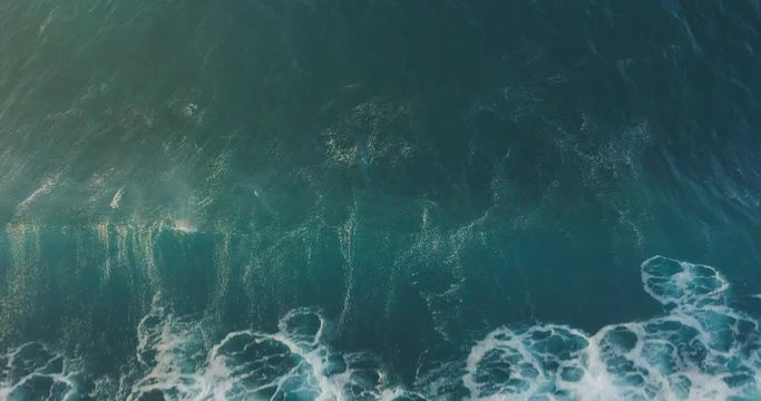 Aerial top down view of a blue breaking wave with ocean white water crashing in motion and foam textures at sunset, golden spray, ocean washing machine