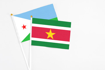 Suriname and Djibouti stick flags on white background. High quality fabric, miniature national flag. Peaceful global concept.White floor for copy space.