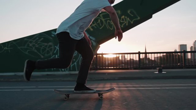skateboarder pushing on bridge in super slow motion in front frankfurt skyline skyscrapers sunset