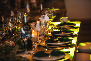 Vintage decoration of reception dinner table. Rustic wedding table setting in fancy European restaurant. Wine glasses, plates, forks and green briefcases for the banquet. Elegant arrangement.