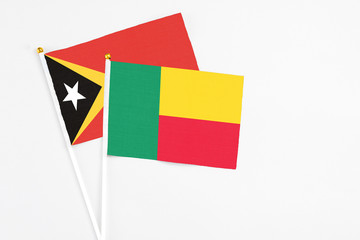 Benin and East Timor stick flags on white background. High quality fabric, miniature national flag. Peaceful global concept.White floor for copy space.