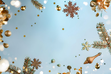 Merry Christmas and New Year background. Xmas holiday card made of flying decorations, gold fir branches, balls, snowflakes, sparkles, confetti, bokeh, light on light blue background. Selective focus