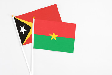 Burkina Faso and East Timor stick flags on white background. High quality fabric, miniature national flag. Peaceful global concept.White floor for copy space.
