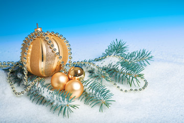 Fototapeta na wymiar Shiny sparkling golden Christmas baubles and trinkets, wintertime arrangement. Abstract winter blue white background with natural fir twigs under snow. Merry Xmas and a Happy New Year!