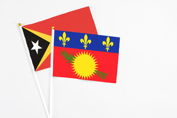 Guadeloupe and East Timor stick flags on white background. High quality fabric, miniature national flag. Peaceful global concept.White floor for copy space.