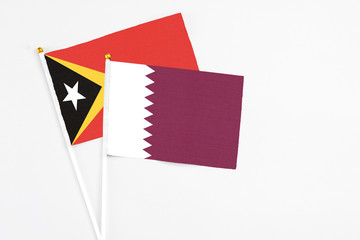 Qatar and East Timor stick flags on white background. High quality fabric, miniature national flag. Peaceful global concept.White floor for copy space.