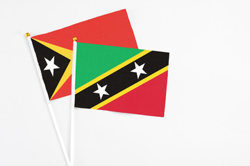 Saint Kitts And Nevis and East Timor stick flags on white background. High quality fabric, miniature national flag. Peaceful global concept.White floor for copy space.