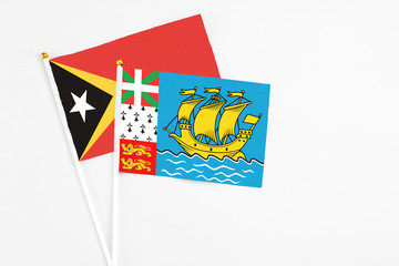 Saint Pierre And Miquelon and East Timor stick flags on white background. High quality fabric, miniature national flag. Peaceful global concept.White floor for copy space.