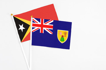 Fototapeta premium Turks And Caicos Islands and East Timor stick flags on white background. High quality fabric, miniature national flag. Peaceful global concept.White floor for copy space.