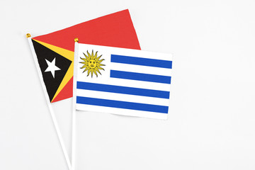 Uruguay and East Timor stick flags on white background. High quality fabric, miniature national flag. Peaceful global concept.White floor for copy space.
