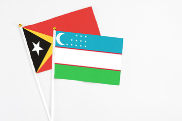Uzbekistan and East Timor stick flags on white background. High quality fabric, miniature national flag. Peaceful global concept.White floor for copy space.