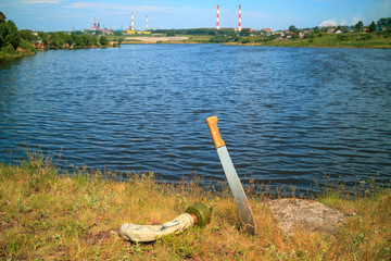 a machete stuck in the ground with grass nearby is a gas mask