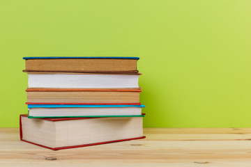 Simple composition of many hardback books, raw of books on wooden table and light green background