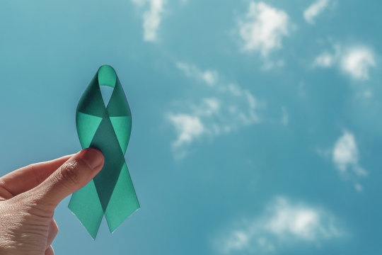Hand holding Teal Ribbon over blue sky, Ovarian Cancer, cervical Cancer, anti bullying and sexual assault awareness