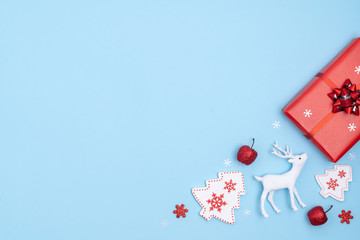 New Year and Christmas frame. Red and white christmas decorations - gift box, stars, christmas tree, deer on pastel blue paper background. Top view, flat lay, copy space
