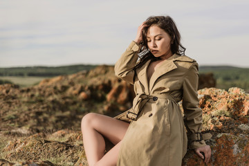 young beautiful brunette in a beige spring coat in the field under the autumn sun. attractive young...