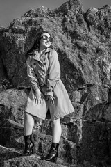 young beautiful brunette girl in spring coat and sunglasses outdoors in autumn sun. attractive young woman in autumn image. monochrome, black and white photography
