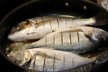 Three marinated gilthhead seabreams roast in a pan