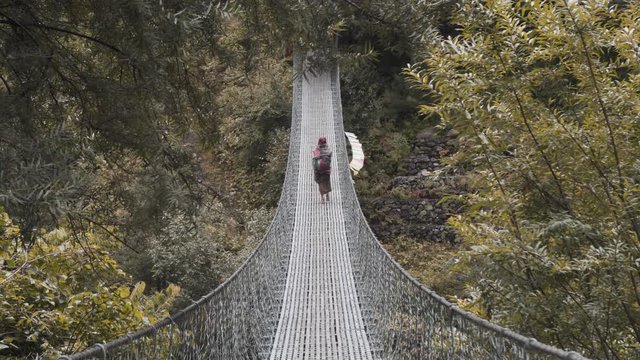 old woman from a nepal village over the himalaya mountain cross a suspension bridge in the middle of the wild forest, annapurna circuit near Manang, Nepal