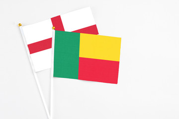 Benin and England stick flags on white background. High quality fabric, miniature national flag. Peaceful global concept.White floor for copy space.