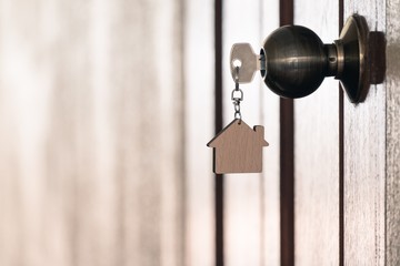 Home key with house keyring in keyhole on wooden door