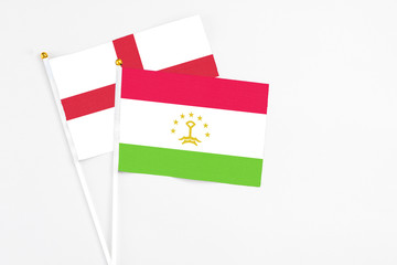 Tajikistan and England stick flags on white background. High quality fabric, miniature national flag. Peaceful global concept.White floor for copy space.
