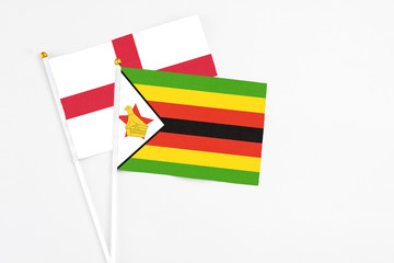 Zimbabwe and England stick flags on white background. High quality fabric, miniature national flag. Peaceful global concept.White floor for copy space.