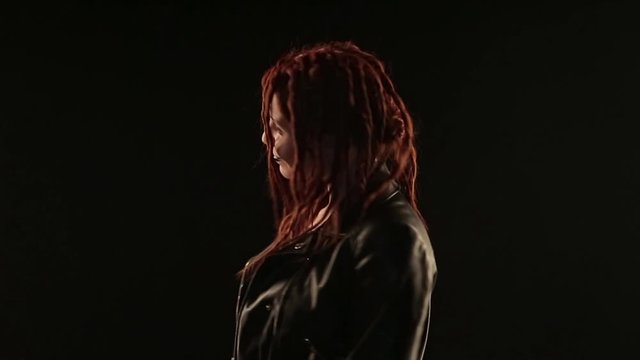 concept dances, parties, advertising leather jackets, styling hair, hairdressing dreadlocks, make-up: dark lipstick. rocker dancing on black background, woman styling red hair