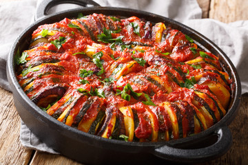 Baked zucchini, potatoes, eggplant and onions in tomato sauce close-up in a pan. horizontal