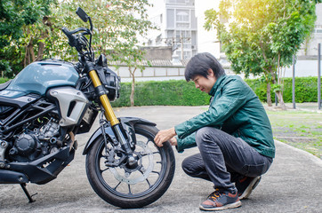 Wheels to take you anywhere. Shot of Handsome rider biker man in green leather jacket checking out wheels and tires of a motorbike at the outdoor