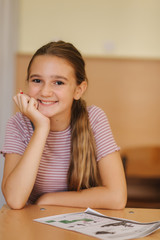Happy schoolgirl sitting at desk and writing in exercise book