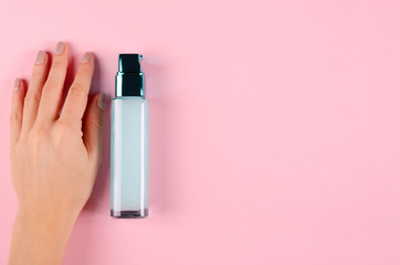 Hand with beauty cream in glass bottle on pink background.