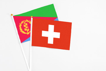 Obraz premium Switzerland and Eritrea stick flags on white background. High quality fabric, miniature national flag. Peaceful global concept.White floor for copy space.