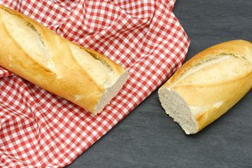 rustic crusty white bread lying on black slate on red white towel in the kitchen