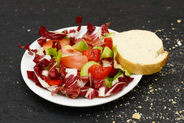 mixed salad and rustic crusty white bread lying on black slate in the kitchen