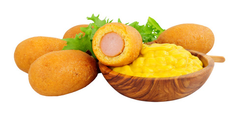 Mini party corn dogs on wooden sticks with a wooden bowl of American mustard isolated on a white background