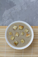 mushroom soup with crackers in a white plate. the view from the top. space for text. soup puree on a gray background. food for lunch. the liquid food. the dish for the restaurant.