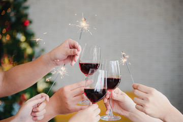Close up people cheers and clinking red wine glass for celebrate holiday event party in christmas tree background