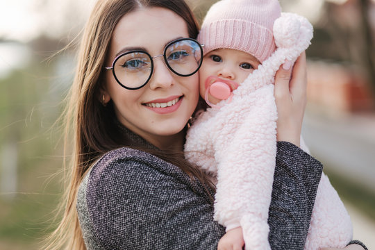 Portrait of mother and her little baby girl. Beautiful mom and cute baby. Mother hud her daughter. Baby dressed in peanch colour hat and nipple toy. Mom kiss her daughter