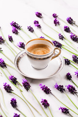 Obraz na płótnie Canvas Cup of fresh americano or espresso coffee with patterned lilac or violet color muscari flowers tiled on white marble table background. Spring or summer morning still life copy space