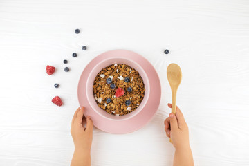 Child's hands holding spoon over table with healthy food. Top view.