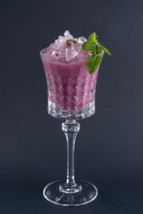 Purple alcoholic cocktail with blueberry and mint leaf isolated on dark background