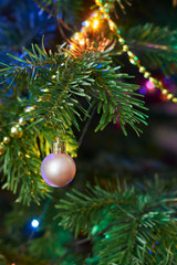 New Year's composition, Christmas decorations. Golden christmas ball hanging on a fir-tree against the background of a luminous Christmas garland