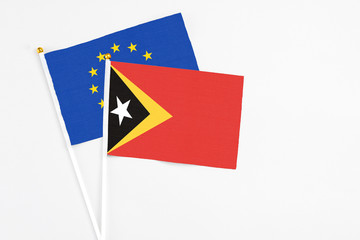 East Timor and European Union stick flags on white background. High quality fabric, miniature national flag. Peaceful global concept.White floor for copy space.