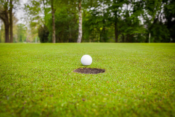 golf ball on lip of cup. Golf ball on green grass in golf course