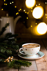 Cup of coffee or eggnog on vintage rustic wooden table with bokeh wreath background, Christmas morning concept decoration, beautiful festive cup with stars, green pine branch