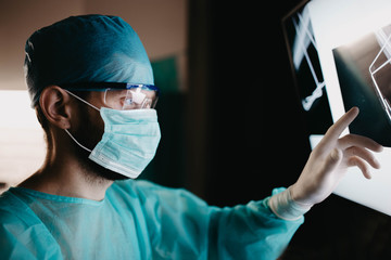 surgeon in uniform and glasses examines an X-ray image of a bone fracture in the operating room.
