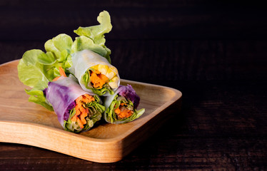 Fresh asian vegetable spring roll wrap with  rice paper with green lettuce, carrot, corn, purple cabbage on wooden plate and table. Clean food, healthy, light appitizer concept. Free copy space on rig
