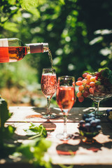 Rose wine tasting, glass of rose wine poured from bottle outdoors in garden party in vineyard, ripe...