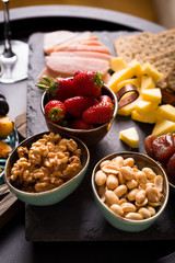 Cheese and fruits plate with glass of white wine on round tray, colorful and delicious charcuterie with snacks and wineglass for romantic evening, wine tasting, selective focus.